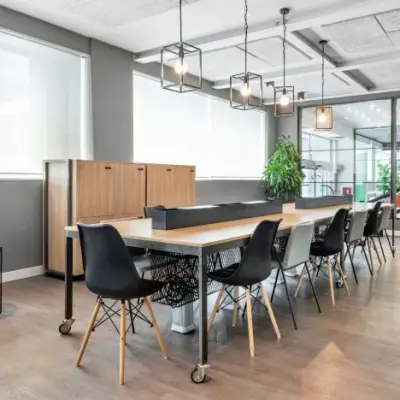 Moderne kantoorruimte met lange tafel en zwarte stoelen op Siriusdreef 17, Hoofddorp. Geschikt voor werkplekken met veel lichtinval door grote ramen. Ideaal om kantoorruimte te huren.