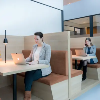 Moderne kantoorruimte op Bargelaan 200, Leiden, met houten tafels en banken, ideaal voor zakelijke meetings. Perfect voor wie kantoorruimte wil huren. Medewerkers werken geconcentreerd op laptops.