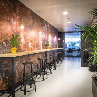 Moderne kantoorruimte huren in Leiden aan de Bargelaan 200 met hoge zitplaatsen, groene planten en een stijlvolle verlichtingswand.