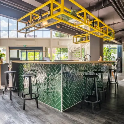 Moderne kantoorruimte op Kanaalpark 140 in Leiden met een stijlvolle bar, groene tegels en gele accenten. Ruim, met veel natuurlijk licht en zitmogelijkheden.