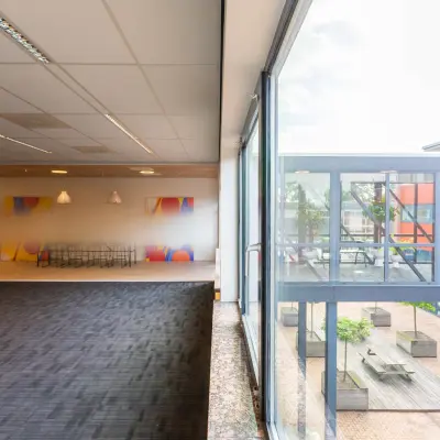 Kantoorruimte huren in Leiden op Pompoenweg 3 - 15, met grote ramen die uitzicht bieden op een binnenplaats. Het interieur bevat een vergaderruimte met kleurrijke achtergrond en een tapijtvloer.