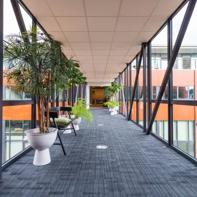 Verlichte corridor in kantoorpand Pompoenweg 3-15 Leiden met grote ramen en planten, ideaal voor kantoorruimte huren.