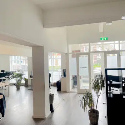 Ruime, lichte kantoorruimte op Wilhelminasingel 44-46 in Maastricht, met meerdere werkplekken te huur. Grote ramen en planten geven de ruimte een frisse uitstraling.