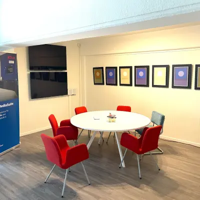 Vergaderruimte in kantoorpand op Wilhelminasingel 44-46 in Maastricht, met rode stoelen rond een witte tafel en kleurrijke kunst aan de muur. Ideaal voor kantoorruimte huren.