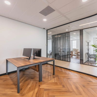 Moderne kantoorruimte te huur met glazen wanden, houten vloer en een bureau met monitor in Rijswijk.