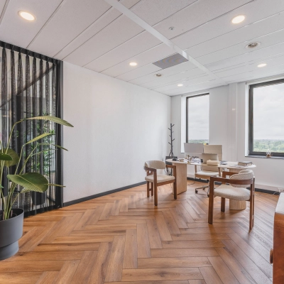 Ruime kantoorruimte met houten vloer en grote ramen in Rijswijk, geschikt om te huren voor zakelijk gebruik. Voorzien van twee bureaus en comfortabele stoelen.