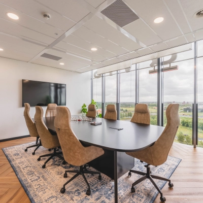 Vergaderruimte met een grote ovale tafel en comfortabele bruine stoelen in een kantoorpand aan de Laan van Zuid Hoorn 70, Rijswijk. De ruimte biedt een mooie blik naar buiten.
