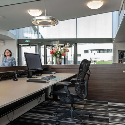 Receptieruimte in een kantoorpand aan Boven de Wolfskuil 3, Roermond, met balie, computerscherm en stoelen. Een persoon staat binnen te kijken vanuit de ingang.