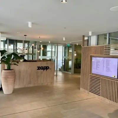 Moderne receptie in kantoorpand aan Bahialaan 100, Rotterdam Brainpark, met grote plantenpot, houten balie en digitaal scherm. Geschikt voor wie kantoorruimte wil huren.