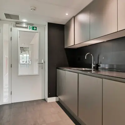 Moderne kitchenette in een kantoorpand aan Coolsingel 104, Rotterdam Centrum. Ideaal voor huur, met strakke grijze kasten en een donkere werkblad voor functies als kantoorruimte huren.