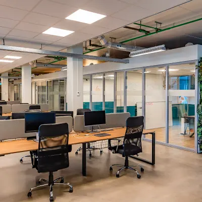 Ruime kantoorruimte met moderne bureaus en stoelen, ideaal om te huren. De ruimte in Rotterdam Delfshaven heeft een groen accent en glazen wanden, wat een open en uitnodigende sfeer creëert.