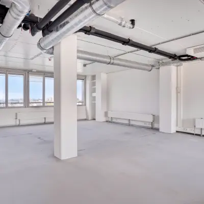 Lichte kantoorruimte op Kratonkade 7 - 27 in Rotterdam Delfshaven, met witte muren, buizen aan het plafond en grote ramen. Ideaal voor kantoorruimte huren.