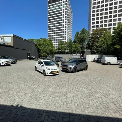 Parkeerplaats naast kantoorpand op Van Helmontstraat 17-23 in Rotterdam Delfshaven, met geparkeerde auto's en omringende hoge gebouwen.