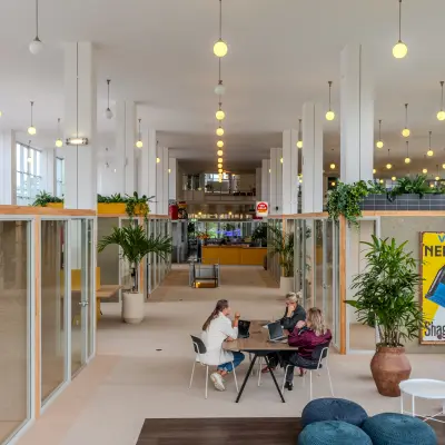 Kantoorruimte huren op Van Nelleweg 1 in Rotterdam Delfshaven met moderne werkplekken, veel licht en planten. Vier personen aan een tafel voeren zakelijke activiteiten uit in een ruim kantoorpand.