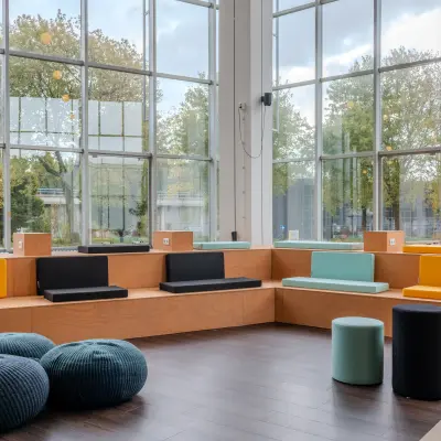 Modern ingerichte kantoorlounge met kleurrijke zitmodules en grote ramen bij Van Nelleweg 1, ideaal voor wie kantoorruimte wil huren in Rotterdam Delfshaven.