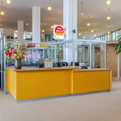Moderne kantoorruimte huren in een helder kantoorpand op Van Nelleweg 1, Rotterdam Delfshaven. Het interieur met glazen wanden en gele accenten biedt een open workspace vibe.