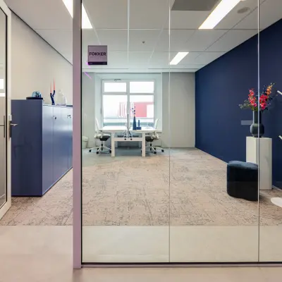 Moderne kantoorruimte huren op Wilhelminaplein 1-40 in Rotterdam Kop van Zuid met glazen wanden, blauwe accenten en wit meubilair. Veel natuurlijke lichtinval en een professionele sfeer voor zakelijke activiteiten.