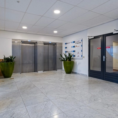 In de entree van het kantoorpand op de Brauwweg 52-66 in Schiedam zijn liften en glazen deuren te zien, met sierplanten voor een uitnodigende sfeer. Ideaal voor kantoorruimte huren.