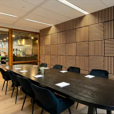 Moderne vergaderruimte in kantoorpand Boeing Avenue 1-19, Schiphol Rijk met houten muren, een lange zwarte tafel en gestoffeerde stoelen.