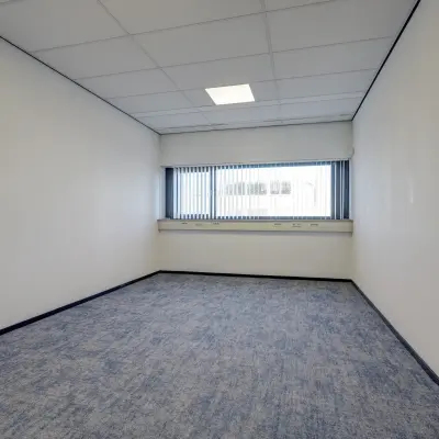 Lege kantoorruimte met blauw tapijt en witgeschilderde muren op Fischerpad 106, Sittard, geschikt voor kantoorruimte huren.