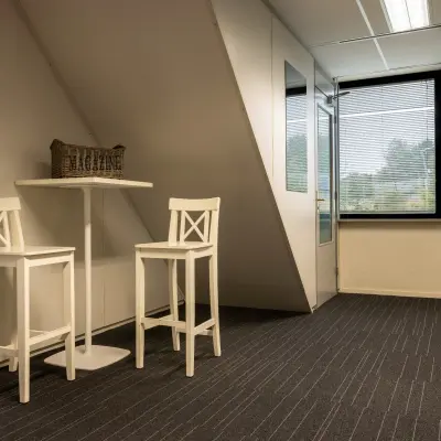 Kantoorruimte huren aan Curieweg 9 in Spijkenisse met twee hoge witte krukken en een tafel, minimalistisch ingericht en geschikt voor zakelijke gesprekken of ontspanning.