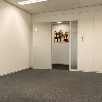 Onthullend kantoorpand op Curieweg 9 in Spijkenisse voor wie kantoorruimte wil huren; de ruimte is ongemeubileerd met tapijt en kunst aan de muur.