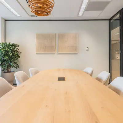 Vergaderruimte in een kantoorpand in Utrecht Centraal Station met houten tafel, comfortabele stoelen en kunst aan de muren.