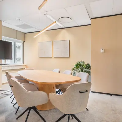 Vergaderruimte in kantoorpand te Utrecht Centraal Station met ovale houten tafel, acht stoelen, en een groot scherm. Neutrale kleuren en natuurlijke verlichting geven een zakelijke sfeer.