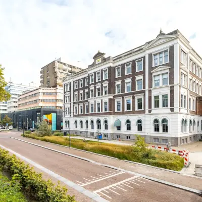 Klassiek vier verdiepingen hoog kantoorpand aan Moreelsepark 1, Utrecht Centraal Station, met bakstenen en witte accenten, omgeven door groene plantsoenen en stedelijke architectuur.
