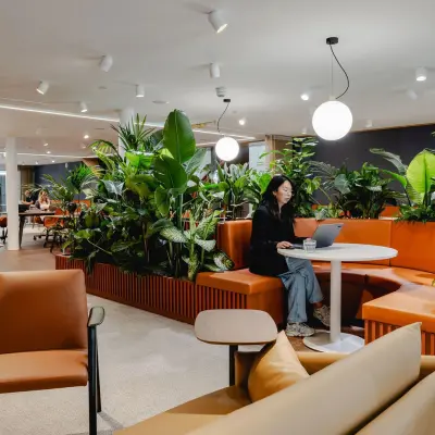 Moderne, gemeubileerde kantoorruimte bij Utrecht Centraal Station met comfortabele zitjes, veel groen en een werkende persoon op een laptop.