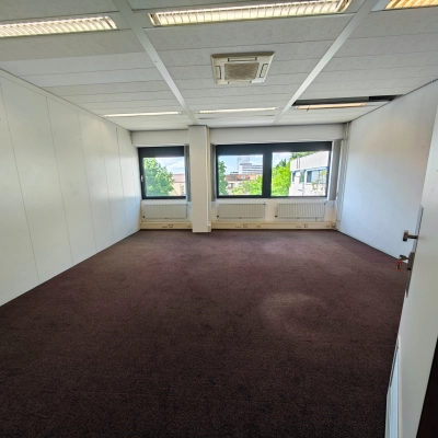 Een lege kantoorruimte op Bernadottelaan 13 in Utrecht Kanaleneiland, geschikt voor huur. Het pand heeft grote ramen die zorgen voor veel daglicht en een warme tapijtvloer.