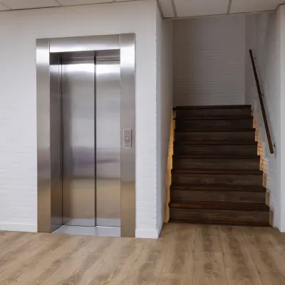 Entree van een kantoorpand met een lift en houten trap, geschikt voor kantoorruimte huren in Utrecht Lage Weide.