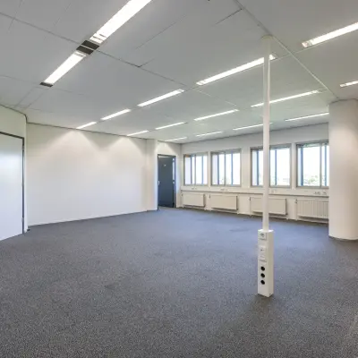 Lichte kantoorruimte in Utrecht Noord met grijze vloerbedekking, grote ramen en twee blauwe deuren langs de wand. Ideaal voor kantoorruimte huren met veel daglicht.
