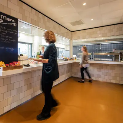 Een lichte pantry in een kantoorpand op Winthontlaan 200, Utrecht Zuid, met een vrouw achter een toonbank met snacks en een passerende persoon. Ideale plek voor kantoorruimte huren.