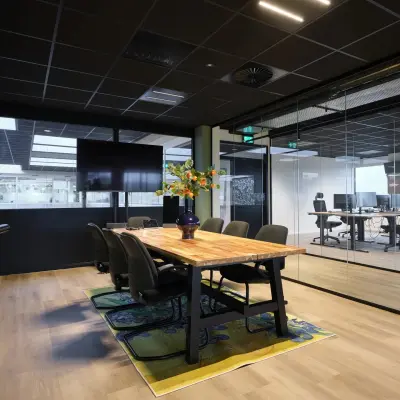 Modern ingerichte kantoorruimte met glazen wanden en houten tafel, gelegen op Havenweg 24 in Vianen Utr, ideaal om een kantoor te huren. Verschillende bureaus zijn zichtbaar door de glazen wanden.