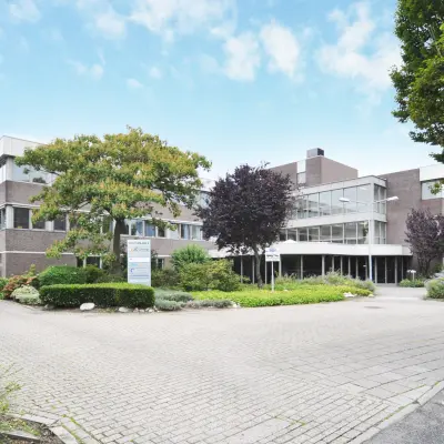 Moderne kantoorgebouw op Houttuinlaan 4 in Woerden, omgeven door groen en ruime parkeerplaats. Geschikt voor bedrijven die kantoorruimte willen huren in een goed bereikbare omgeving.