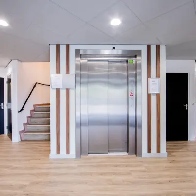 Ingang van een kantoorpand in Woerden op Pelmolenlaan 16, met een lift en trap. Sfeervol verlicht met houten accenten. Kantoorruimte huren mogelijk.