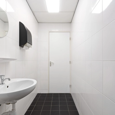 Minimalistische ruimte met witte tegels en wastafel in een kantoorpand aan Stationsplein 4, Zwijndrecht. Ideaal voor bedrijven die kantoorruimte willen huren zonder poespas.