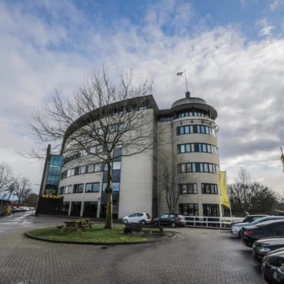 Het ronde kantoorpand op Hanzelaan 351-361 in Zwolle met parkeerplaatsen en een blauwe lucht op de achtergrond.